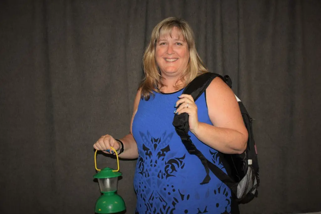 Denise Tyree-Montecino with a backpack holding a green lantern against a dark backdrop.