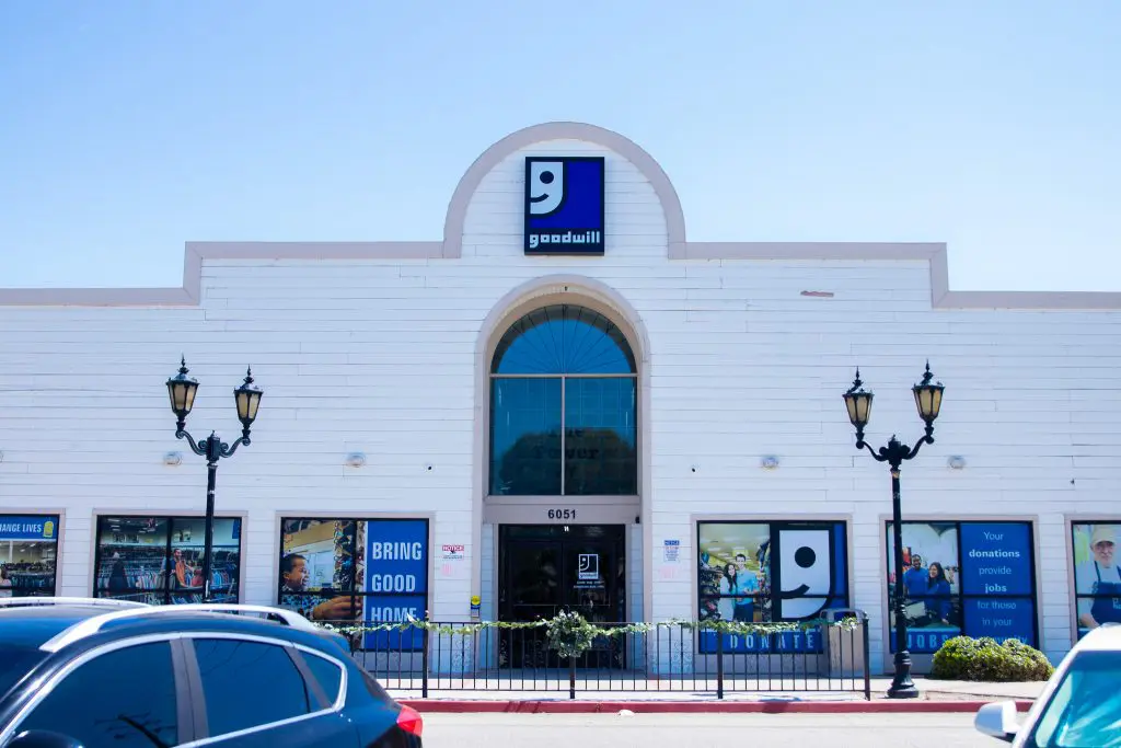 Goodwill White Lance location. A white Goodwill store building with large windows, decorative lamps, and the Goodwill logo above the main entrance. Cars are parked in front.