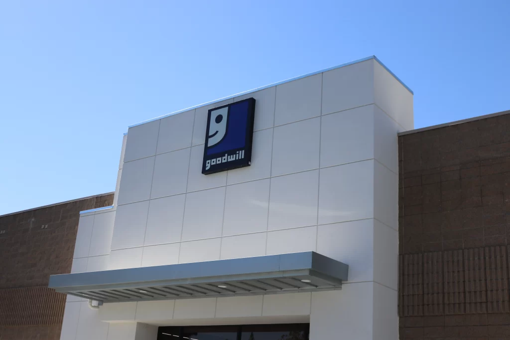 Exterior of a Goodwill store with a square blue and white sign featuring the Goodwill logo and name above the entrance.