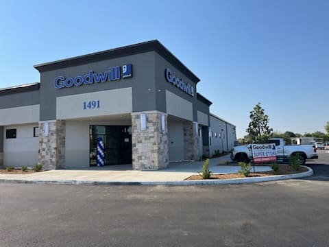 Image of a Goodwill store with a sign reading "1491" above the entrance. The building features a modern design with stone accents. A banner on the side reads "Goodwill Super Store.