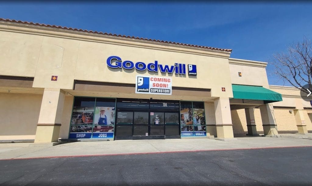 Front view of a Goodwill store under construction, with a banner reading "Coming Soon! Superstore!" above the entrance. The building is beige with a red tile roof and green awnings on the sides.